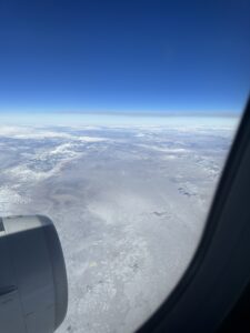 an airplane window with snow covered land and blue sky