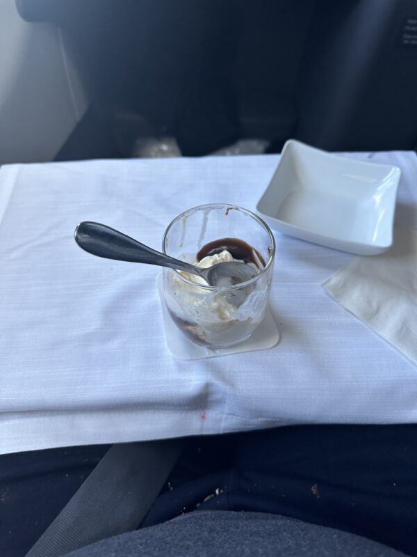 a spoon in a glass cup with ice cream and a plate on a white cloth