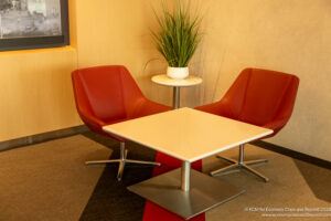 a white square table with red chairs and a plant on it