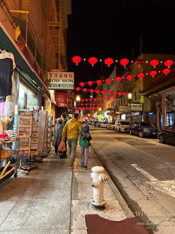 a street with red lanterns and people walking on the sidewalk