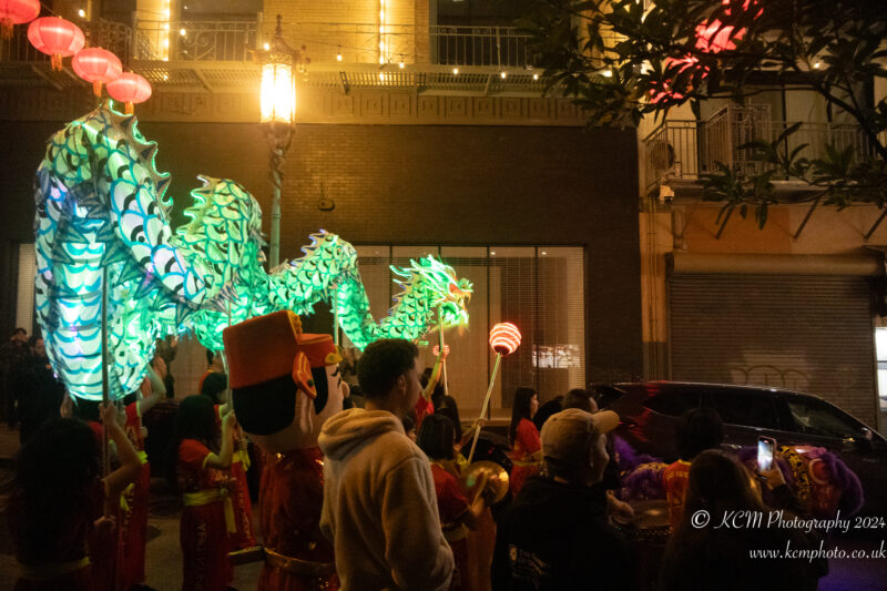 a group of people in clothing holding up a green dragon