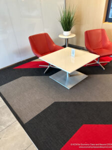 a white square table with red chairs and a plant on a rug
