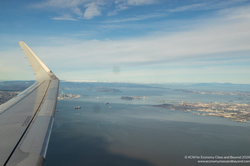 an airplane wing and water with land and buildings in the background