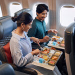 a man and woman eating food on an airplane