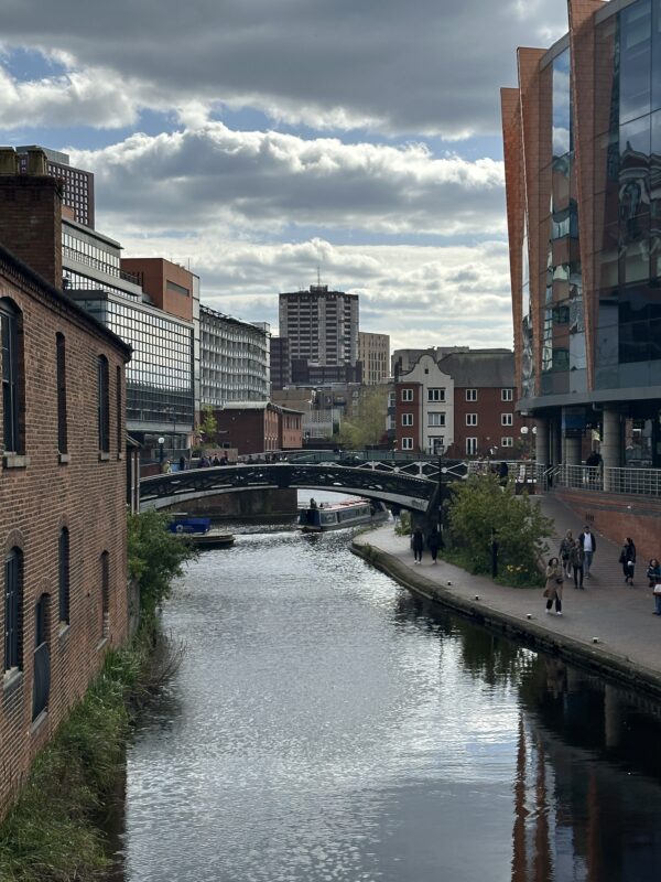 a river between buildings with a bridge and people walking