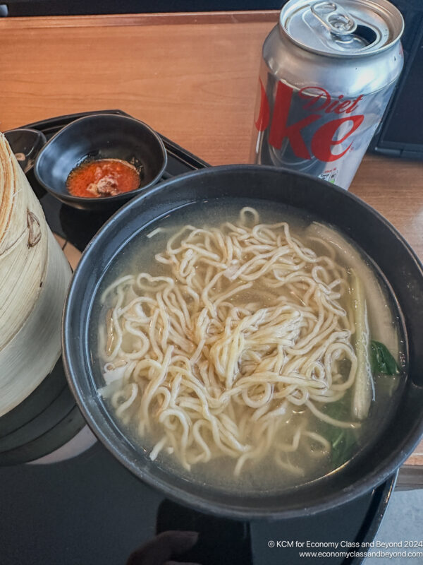 a bowl of noodle soup next to a can of soda