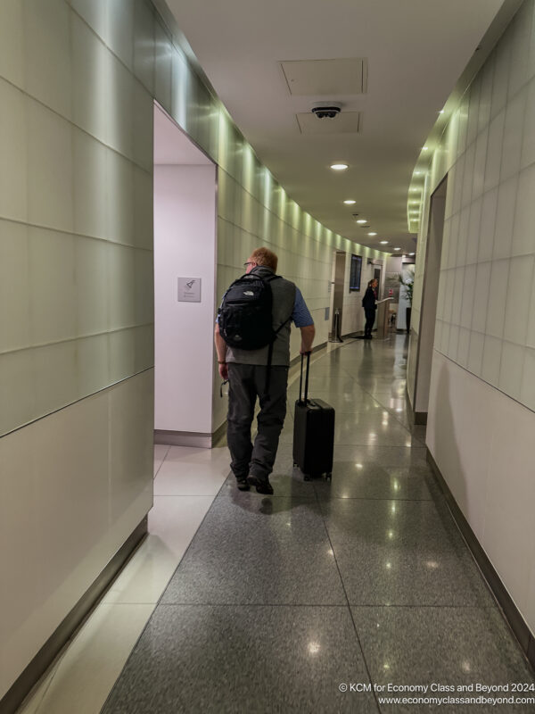 a man with a backpack walking down a hallway with a suitcase