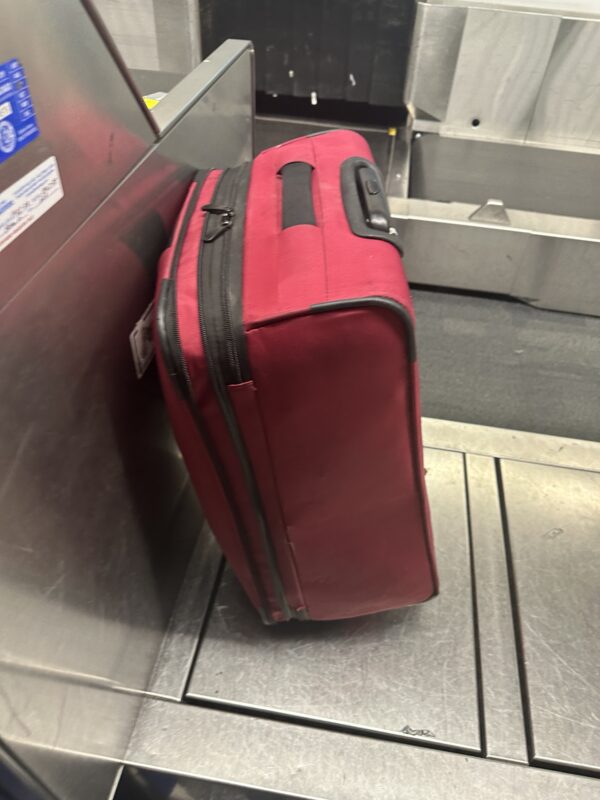 a red suitcase leaning against a machine