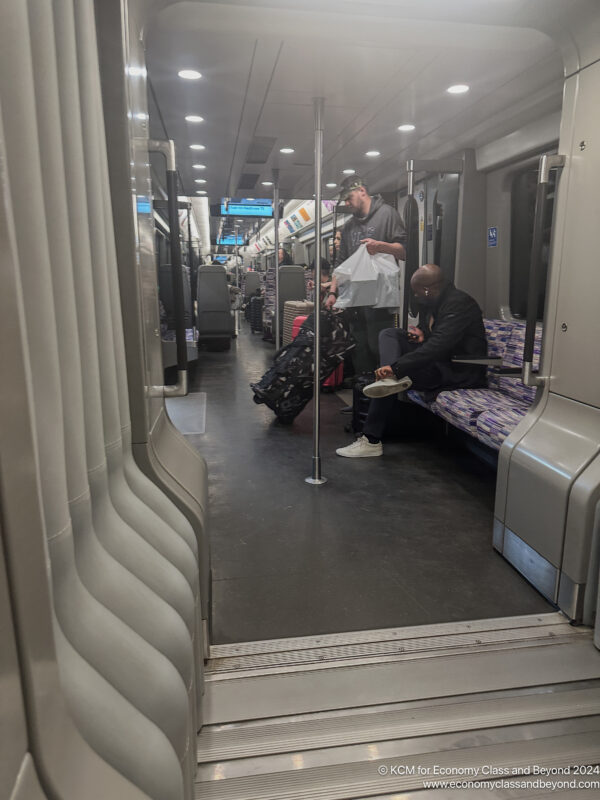 a man standing next to a man sitting on a bench in a train