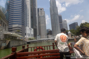 a man standing on a boat in front of a river with tall buildings in the background