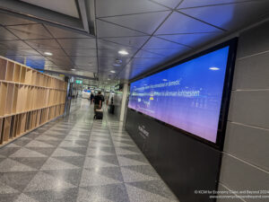 a man walking in a hallway with a large screen