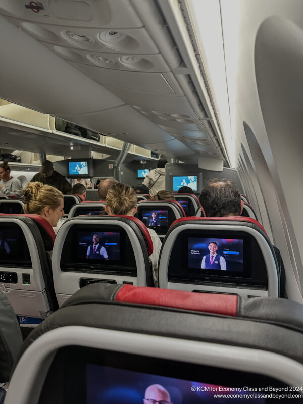 a group of people sitting in an airplane with tv screens