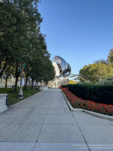 a walkway with trees and a metal sphere in the background