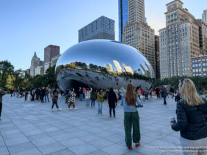 a group of people standing around a large silver object with Millennium Park in the background