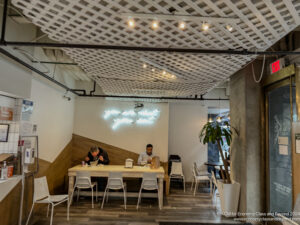 people sitting at a table in a room with white chairs and a plant