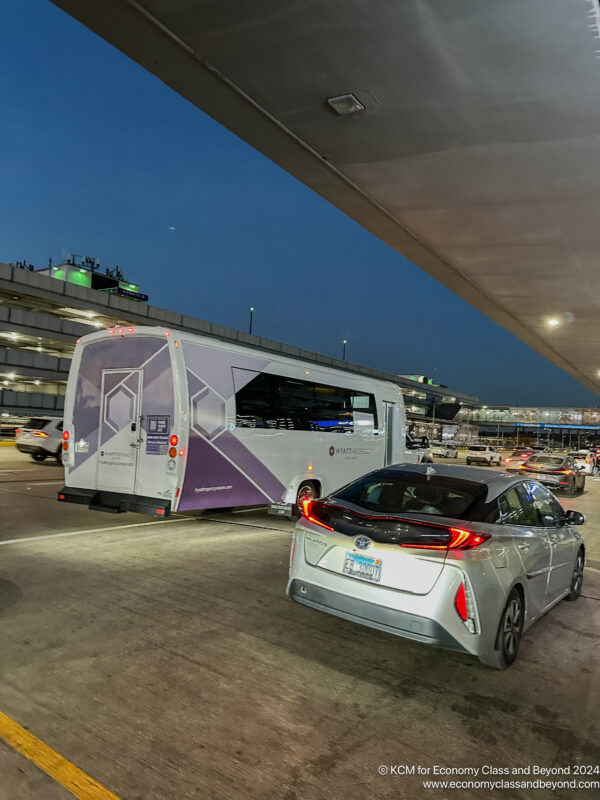 a silver car and bus parked under a bridge