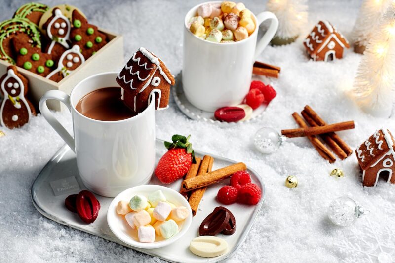 a gingerbread house in a mug of hot chocolate with marshmallows and other treats