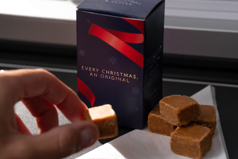 a hand holding a small cube of brown candy next to a box