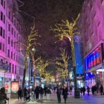 a group of people walking on a sidewalk with trees with lights