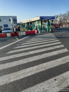 a crosswalk with a sign and people standing in front of it