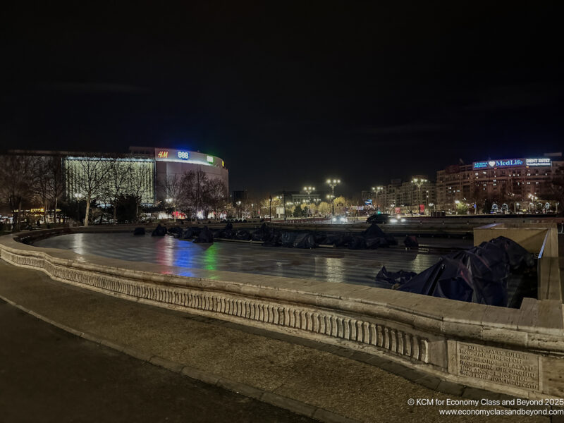 a city at night with a fountain and buildings