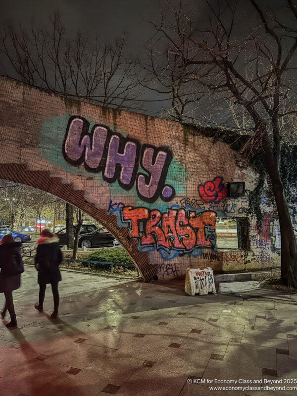 a group of people walking under a brick wall with graffiti