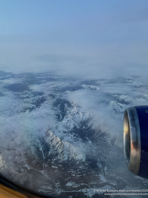 an airplane wing with a jet engine and snow covered mountains