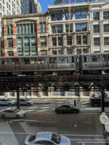 a train on a bridge over a street with cars and buildings