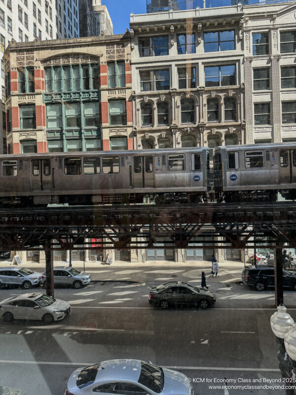 a train on a bridge over a street with cars and buildings