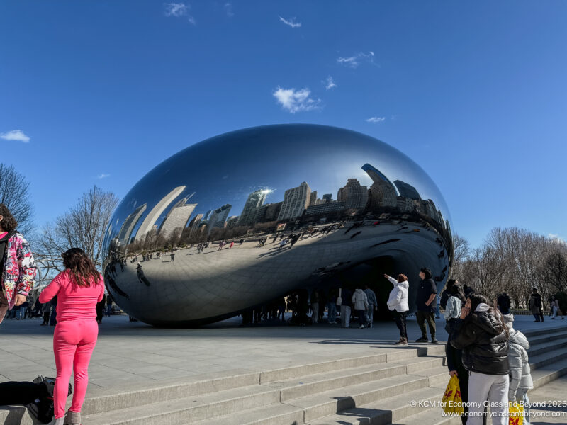 a group of people standing around a reflective object with Millennium Park in the background