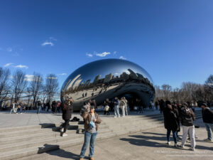 a group of people standing around a large silver object with Millennium Park in the background