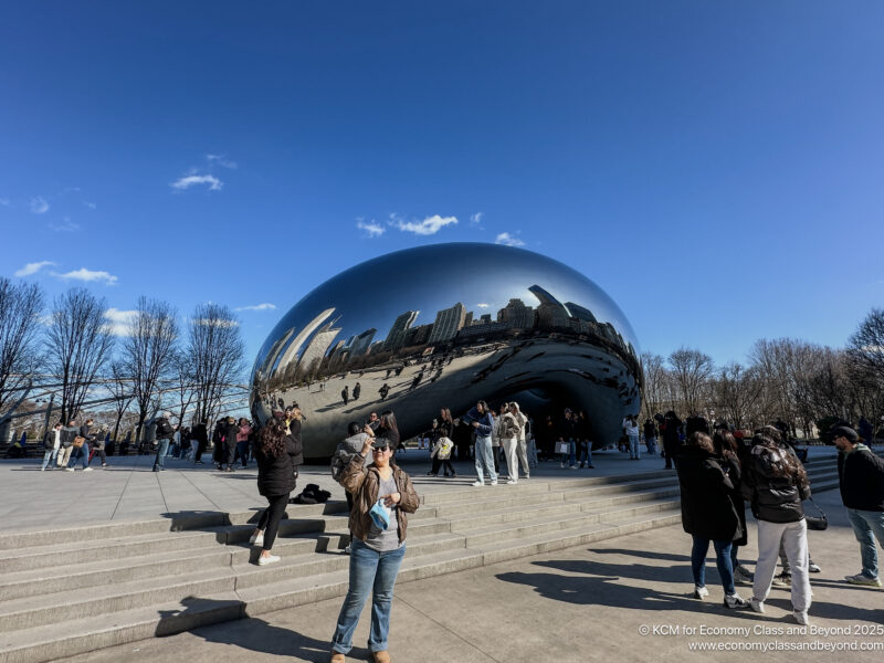 a group of people standing around a large silver object with Millennium Park in the background