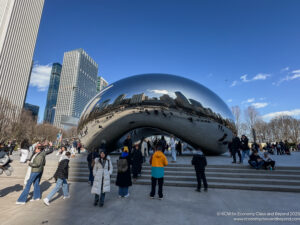 a group of people standing around a large silver object with Millennium Park in the background