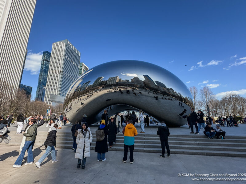 a group of people standing around a large silver object with Millennium Park in the background