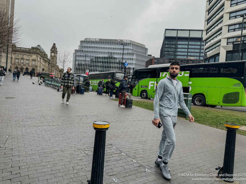 a man walking on a sidewalk with other people and buses