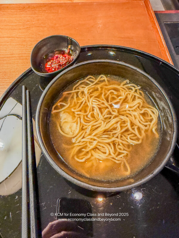 a bowl of noodles with sauce and chopsticks on a black plate