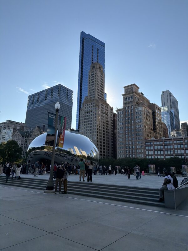 a group of people in a park with a large reflective sculpture
