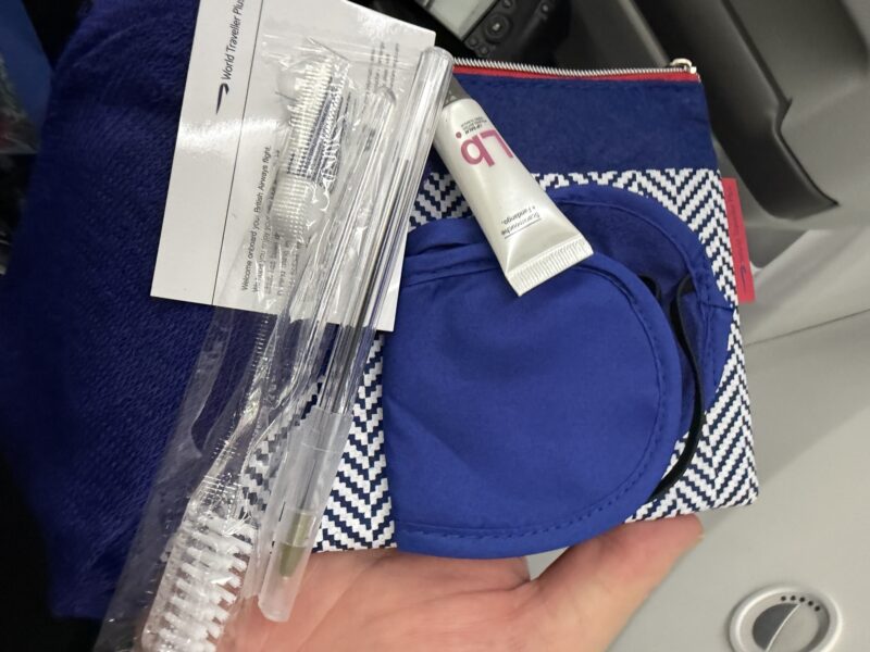 a hand holding a blue and white bag with a toothbrush and a toothpaste