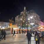 a crowd of people walking around a christmas tree
