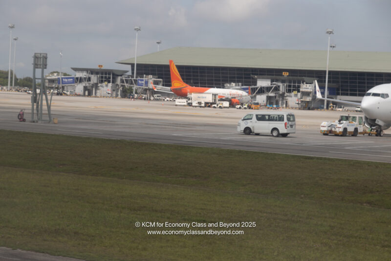 a white van on a runway with an airplane in the background