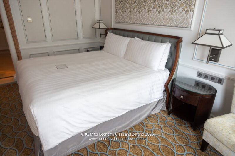 a bed with white sheets and a lamp on the floor