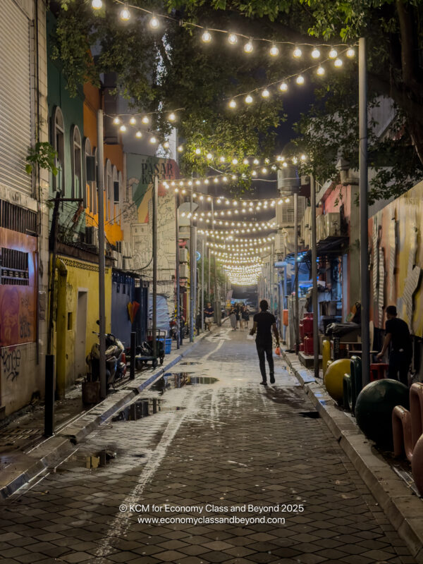 a person walking down a narrow street with lights from the ceiling