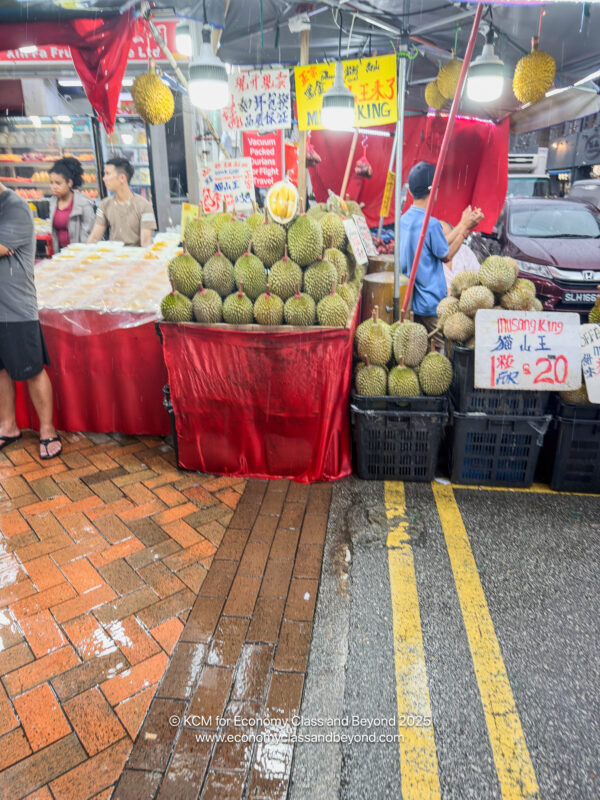 a fruit stand with people standing in front of it