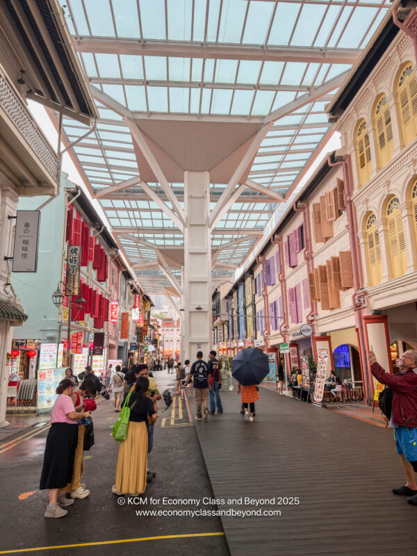 a group of people walking down a street with buildings and a glass roof