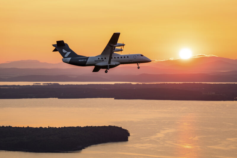 Heart Aerospace’s battery-electric X1 demonstrator banks east toward the rising sun during its first flight near Plattsburgh, New York, in August 2026, with Lake Champlain in the distance.